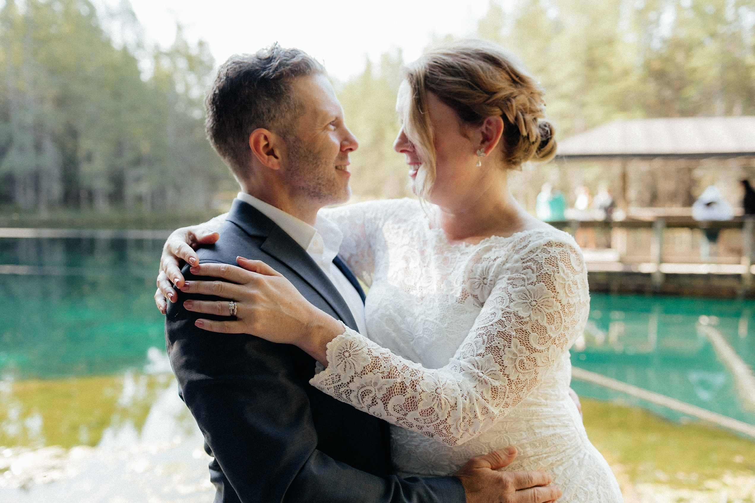 bride and groom standing in front of Kitch-iti-kipi also known as Big Springs. Blue water and a raft in the background