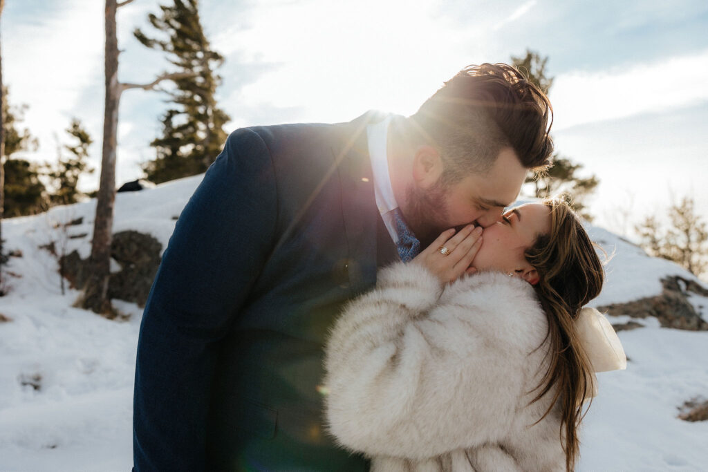 bride and groom kissing, wearing a fur coat with the sun peaking behind them