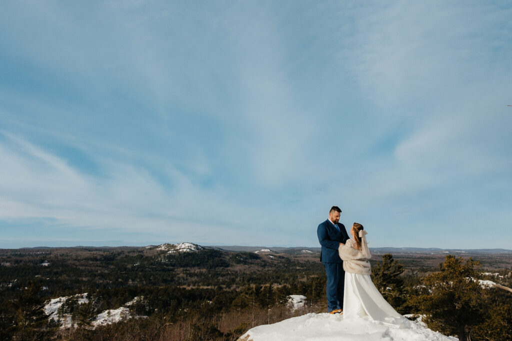 bride and groom standing on top of a mountain, blue sky and snow in the background